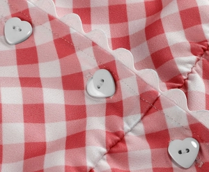 Detail of red gingham dress with scalloped white trim and heart-shaped buttons