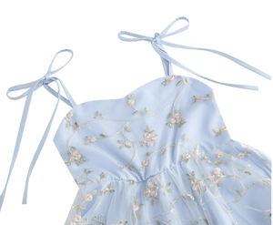 Détail d'une robe en tulle bleu clair avec broderie florale et bretelles à nœuds sur blanc