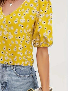 Detail of women's yellow floral V-neck blouse with daisy print and puff sleeves