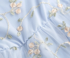 Gros plan sur le tulle bleu clair avec broderie florale délicate et plis doux du vêtement