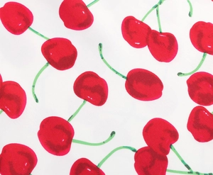 Detailed close-up of summer dress fabric featuring vibrant red cherry prints on white cotton
