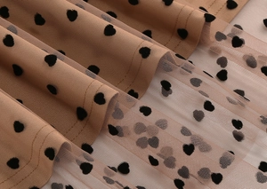 Detail of tan mesh skirt featuring black flocked heart patterns and layered stitching