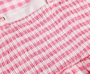 Close-up of pink gingham fabric with smocking detail and metal ring on long dress