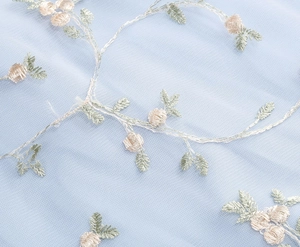 Vue macro d'une broderie florale délicate sur tulle bleu clair avec détails de fleurs 3D