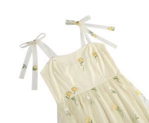 Detail of floral embroidery and mesh ribbon shoulder straps on a light cream summer dress