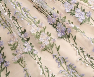 Close-up of intricate floral embroidery in lilac and green on fine beige mesh fabric