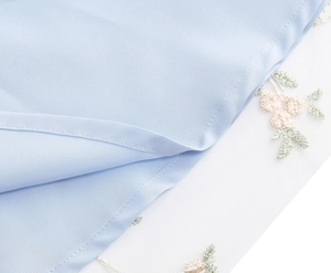 Détail du tissu bleu clair avec broderie de fleurs roses et empiècement en tulle blanc
