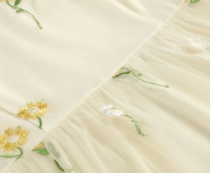 Detailed view of yellow daisy embroidery on delicate off-white mesh tulle fabric