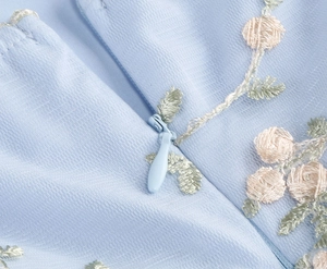 Détail macro de la robe en tulle bleu clair avec broderie rose et fermeture invisible