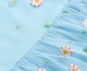 Macro detail of light blue mesh fabric with delicate daisy embroidery and pleated layers