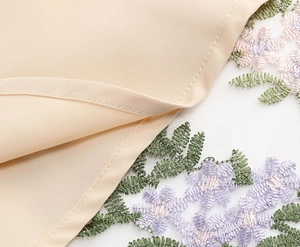 Macro shot of delicate floral embroidery on fine mesh layered over woven fabric dress