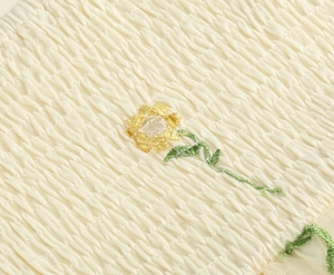 Macro detail of sunflower embroidery on beige smocked fabric of the mesh dress