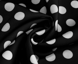 Dettaglio del tessuto a pois bianco e nero che mostra la consistenza liscia e il drappeggio