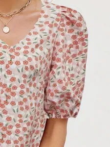 Detail of V-neck floral blouse featuring puff sleeves and elastic cuffs with gold necklace