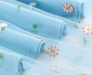 Detail of light blue mesh fabric with delicate daisy embroidery and soft double-layered texture
