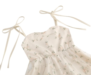 Détail de broderie florale sur robe en tulle beige avec bretelles à nœuds et plissée