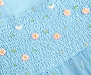 Macro shot of light blue smocked fabric with detailed daisy embroidery and mesh details