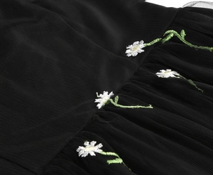 Detailed close-up of white daisy embroidery on delicate black mesh fabric dress