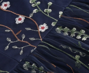 Close-up of intricate floral daisy embroidery on navy blue mesh fabric with elegant pleats