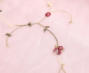 Detail aus rosa Netzstoff mit exquisiter roter Blumenstickerei und grünem Blattmuster