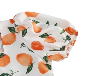 Detail of girl's white dress with orange fruit print and elastic puff sleeve cuffs