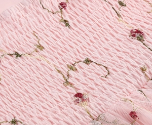 Detail aus rosa gesmoktem Stoff mit feiner roter Rosenstickerei und floralen Texturen