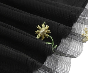 Close-up of yellow daisy floral embroidery on black mesh fabric with delicate craftsmanship