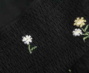 Macro detail of daisy embroidery on black smocked fabric texture for maxi dress