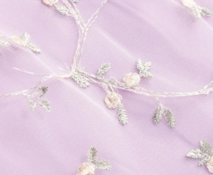 Détail du tissu en maille lavande avec broderie florale et détails de fils argentés