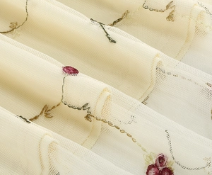 Makroaufnahme filigraner Blumenstickerei auf cremeweißem Vintage-Mesh-Kleiderstoff