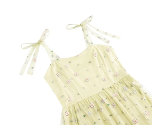 Detail of light yellow floral dress featuring delicate daisy embroidery and bow straps