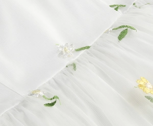 Close-up of white mesh fabric featuring delicate yellow floral embroidery and greenery