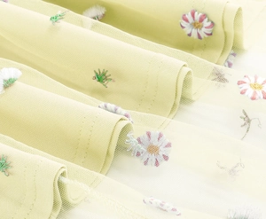 Close-up of delicate floral embroidery on light green semi-transparent mesh fabric