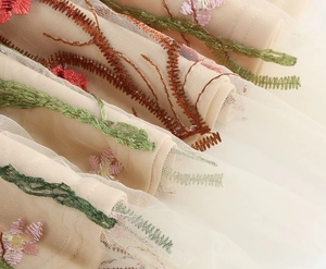 Detailed close-up of colorful floral embroidery on light beige mesh fabric