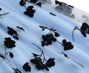 Close-up detail of light blue fabric with black floral flocking mesh on girl dress