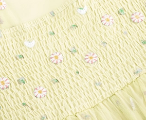 Detail of floral daisy embroidery and smocking texture on a French mesh strap dress