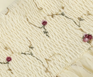 Detail aus cremefarbenem Stoff mit floraler Stickerei, Plissee und Spitzenbesatz