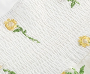 Detail of white shirred fabric with yellow sunflower embroidery and green leaves