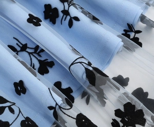 Detail of light blue mesh fabric with 3D black flocked floral patterns on a girl's dress
