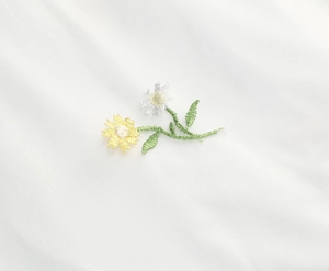 Detailed close-up of intricate daisy embroidery and green leaves on white mesh fabric
