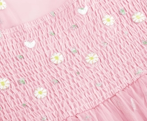 Close-up of pink smocked fabric featuring delicate white daisy embroidery and mesh detail
