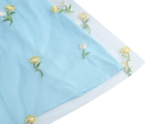 Detail of delicate daisy embroidery on light blue mesh tulle fabric for a floral dress