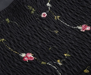 Detail der Smocking-Textur mit feiner Rosenstickerei auf einem schwarzen Kleidungsstück