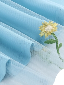 Close-up of intricate sunflower embroidery on light blue mesh fabric layered dress