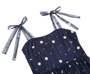 Detail of adjustable mesh bow straps and daisy floral embroidery on navy dress