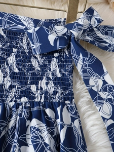 Détail d'une robe fleurie bleue avec bustier smocké et bretelles nouées sur un cintre