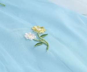Detailed view of yellow and white floral embroidery on light blue tulle mesh fabric