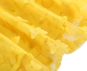 Dettaglio del tessuto a rete giallo con farfalle 3D e ricami dorati sulla gonna lunga