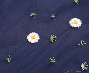 Macro detail of delicate floral daisy embroidery on dark blue fabric texture