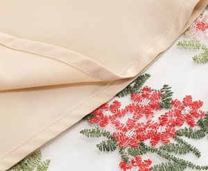 Detail of floral embroidery on sheer mesh fabric with beige double-layered hemline